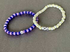 two bracelets with letters on them sitting next to each other in front of a gray surface