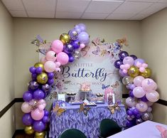 the balloon arch is decorated with purple, gold and white balloons for a little butterfly birthday party