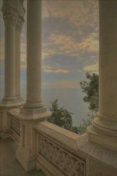 the view from an old building with columns and pillars overlooking the water in the distance