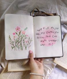 a hand holding an open book with writing on it and pink flowers in the pages