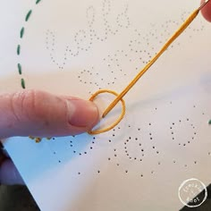 a person is stitching with yellow thread on white paper and has their finger pointing at the string