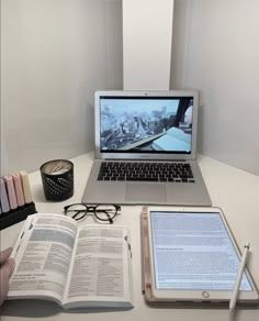 an open laptop computer sitting on top of a desk next to a book and pen