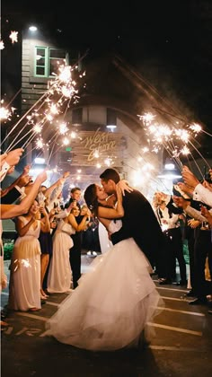 a bride and groom kissing in front of their guests with sparklers at the end