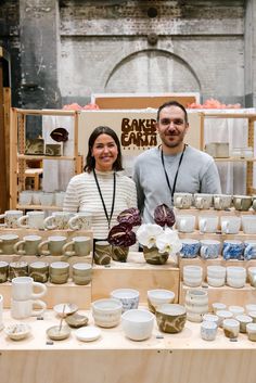 two people standing behind a table full of pottery