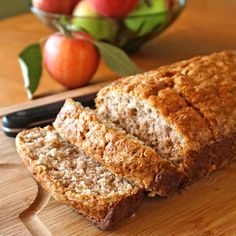 sliced loaf of bread sitting on top of a wooden cutting board with apples in the background