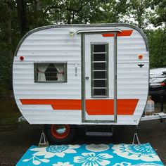 an orange and white trailer is parked on the ground next to a blue rug with flowers