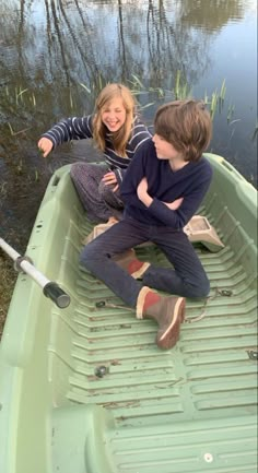 two children are sitting in a green boat on the water and one boy is pointing at something