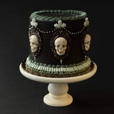 a black and green decorated cake with skulls on the top is sitting on a pedestal