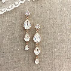 two pairs of crystal earrings sitting on top of a piece of cloth next to a lace