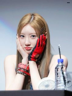 a woman with long hair and red gloves sitting at a table in front of a water bottle