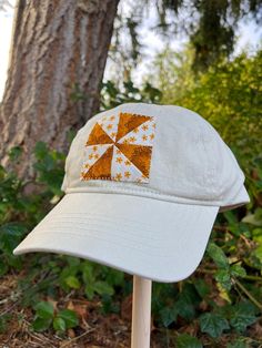 a white hat with an orange and yellow patchwork design on it sitting next to a tree