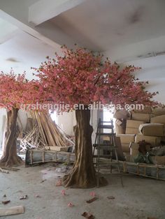 a tree with pink flowers is in the middle of a room filled with chairs and ladders