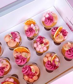 twelve cupcakes with pink frosting and flowers on them in a white box