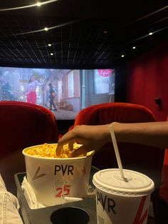 a person is holding a plastic cup with popcorn in it while watching movies on the screen