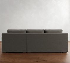 a gray couch sitting on top of a wooden floor next to a white wall in an empty room