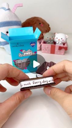 two hands holding small candy bars in front of stuffed animals on a white table top