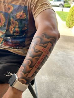 a man with a cross tattoo on his arm sitting in a chair next to a street