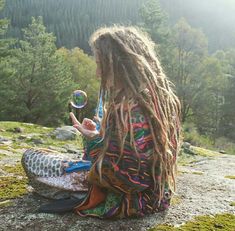 a woman with dreadlocks sitting on top of a hill blowing bubbles in the air