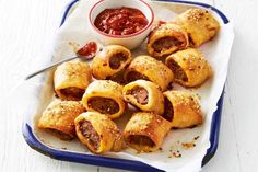 several sausage rolls on a plate with ketchup and dipping sauce in the background