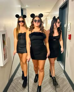 three women dressed up in mickey mouse ears and black dresses are walking down the hallway