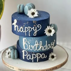 a three tiered blue birthday cake with white daisies on top and the words happy birthday papa written on it