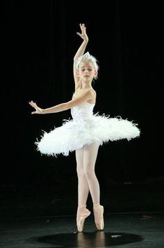 a young ballerina in white tutu and feathered skirt, standing on stage