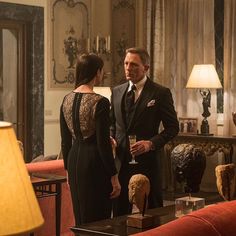 a man and woman standing in a living room talking to each other while holding wine glasses