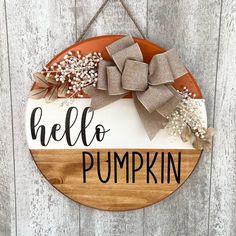 a wooden sign that says hello pumpkin hanging on a wall with a bow around it