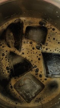 some ice cubes are in a metal pot with water on the side and brown liquid