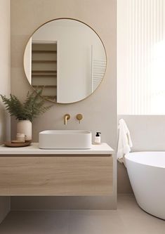 a white bath tub sitting next to a sink under a round mirror in a bathroom