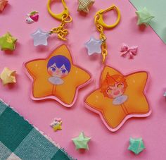 two star shaped key chains sitting next to each other on a pink surface with stars