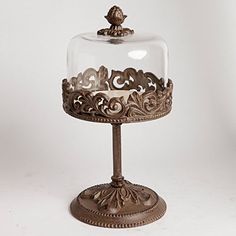 an ornately decorated cake stand under a clochet glass dome on a white background