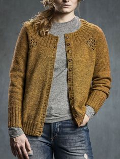 a woman wearing a yellow cardigan sweater and ripped jeans, standing in front of a gray background