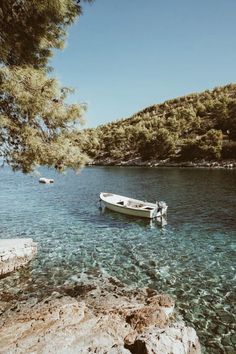 a small boat floating on top of a lake next to a rocky shore covered in trees