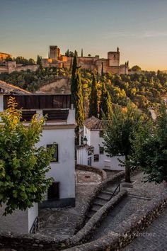 the sun is setting over an old town with stairs leading up to buildings and trees