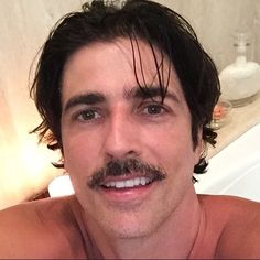 a shirtless man with a mustache and no shirt on in a bath room next to a sink