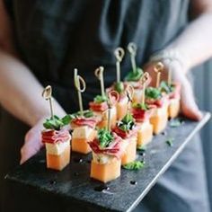 several small appetizers are arranged on a black platter with toothpicks and garnishes