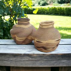 two brown vases sitting on top of a wooden table in front of a bush