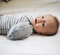 a baby laying on top of a bed next to a white sheet covered ground and looking up at the camera