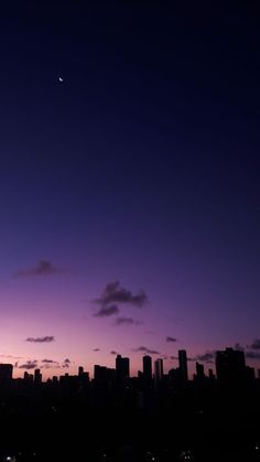 the sky is purple and blue as the sun sets in the distance with buildings silhouetted against it