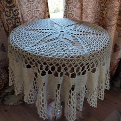 the table is covered with crocheted doily and sits in front of curtains