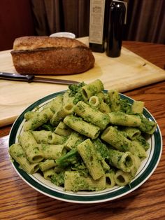 a plate full of pasta and broccoli on a wooden table next to bread