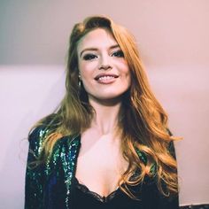 a woman with long red hair wearing a black top and green sequins jacket