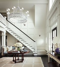 an elegant staircase with chandelier and flowers in vases on the end table