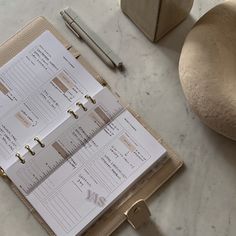 an open planner sitting on top of a table next to a pen and paper holder