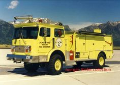 a yellow fire truck parked on top of a tarmac with mountains in the background