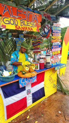 a man standing behind a food stand with bananas and other foods on it's counter