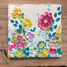 a painted canvas with flowers on it and paintbrushes next to it, sitting on a wooden surface