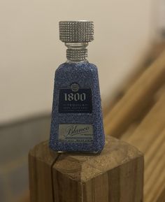 a bottle of blue liquid sitting on top of a wooden block in front of a white wall