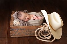 a newborn baby sleeping in a wooden crate with a cowboy hat